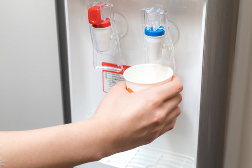 ウォーターサーバーから紙コップに冷たい水を注ぐ