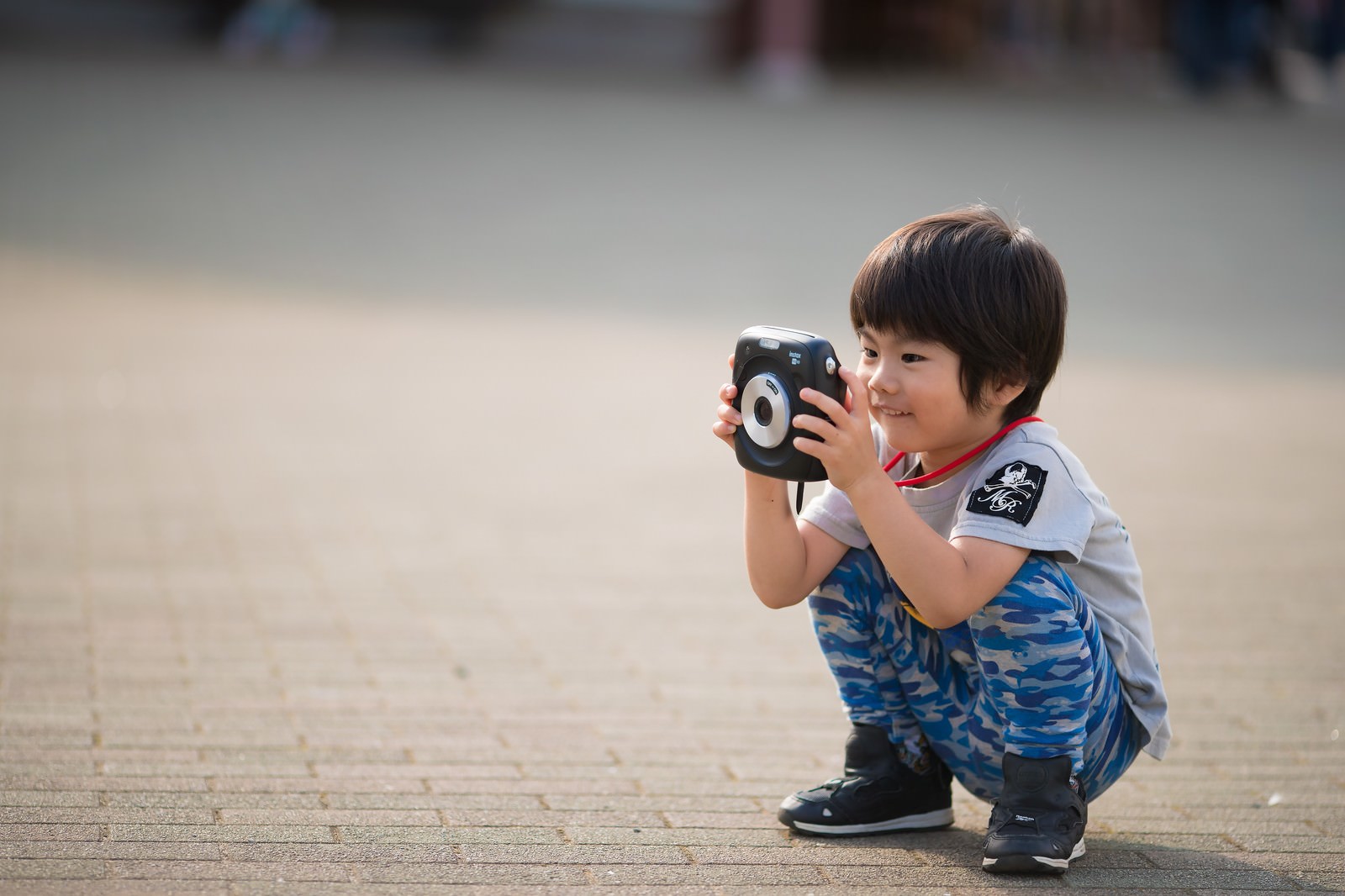 青いシャツを着た子供がインスタントカメラを構えている様子