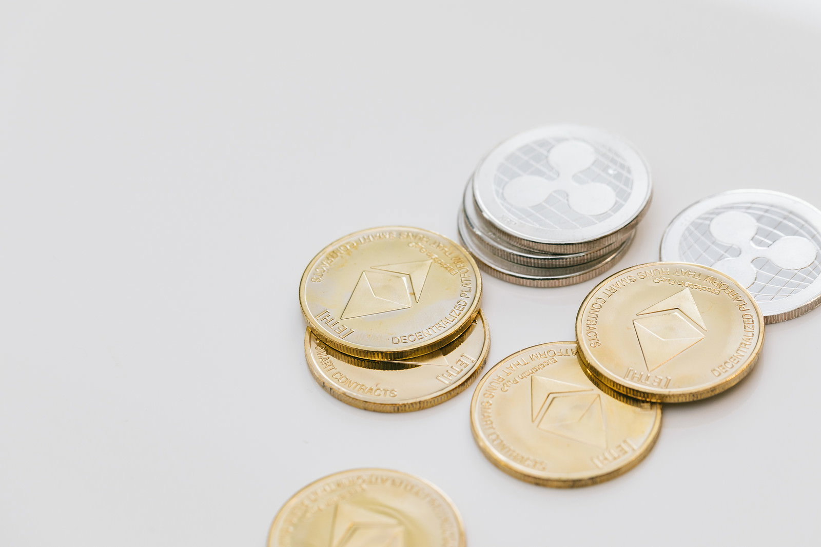 白い背景に置かれたETH（イーサリアム）とXRP（リップル）の金貨と銀貨