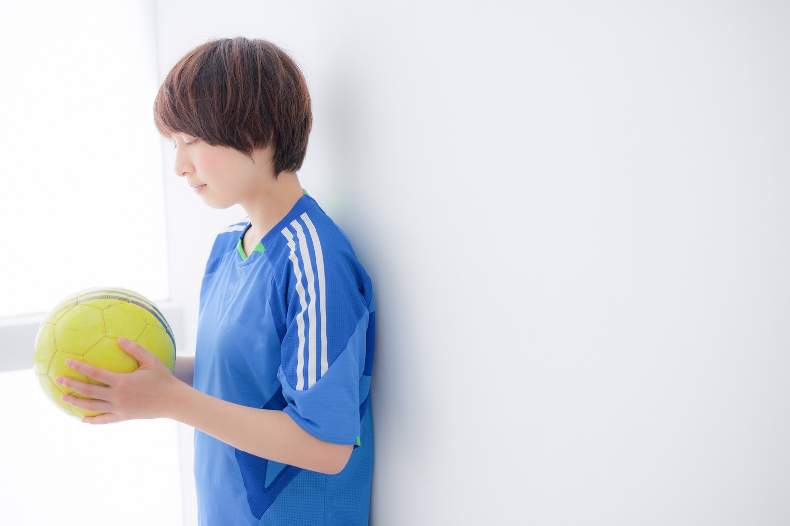 黄色いサッカーボールを持つ青いユニフォーム姿の女性［モデル：八木彩香］