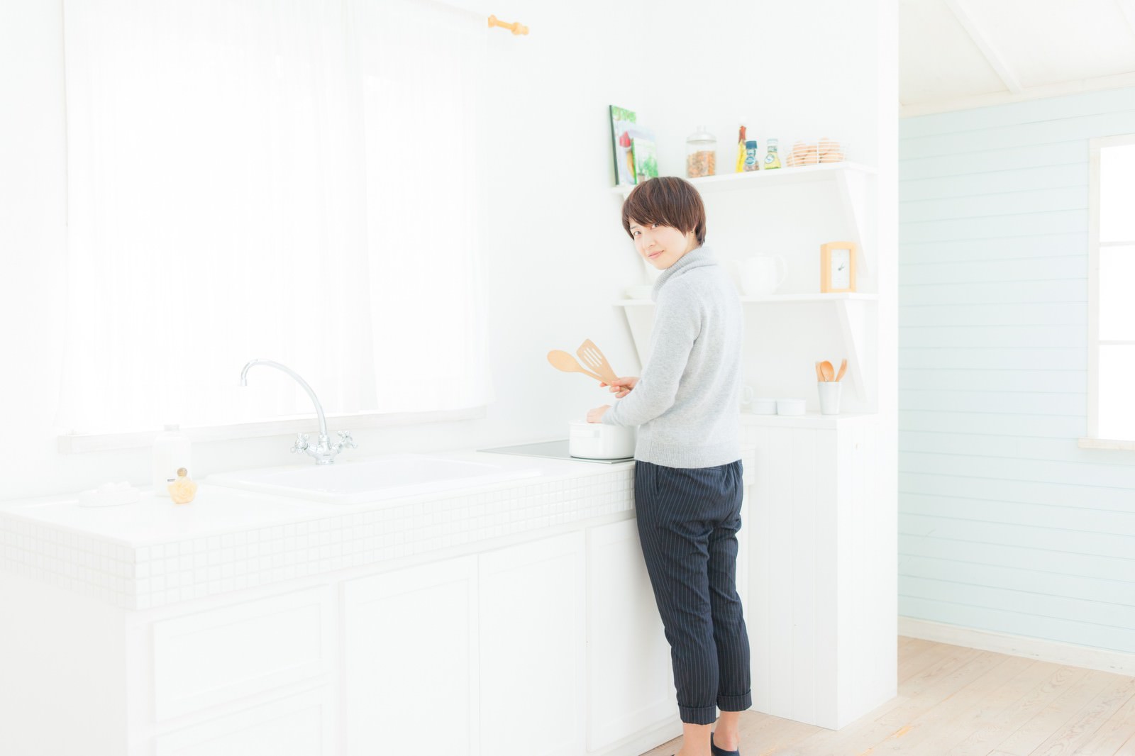 明るいキッチンでエプロンを着けて料理をする女性［モデル：八木彩香］