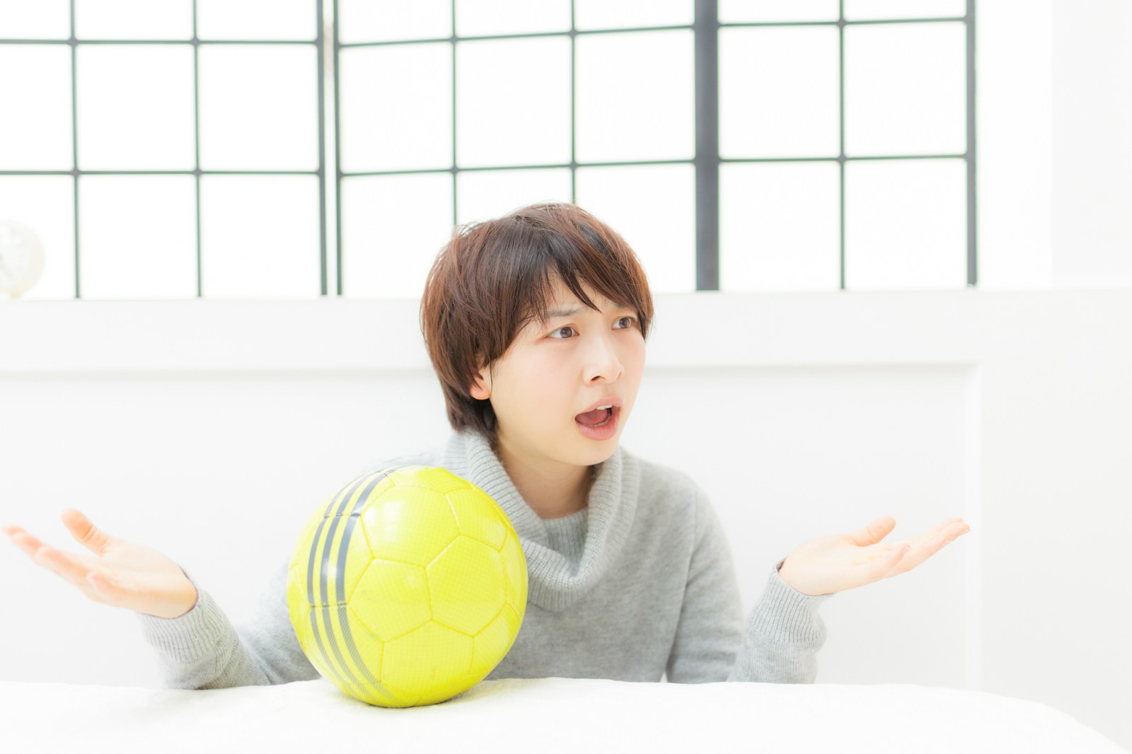 サッカーボールを持って両手を広げ、困惑した表情の女性［モデル：八木彩香］