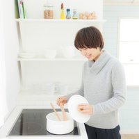 キッチンの IH調理器でスープを温めなおしている女性の写真