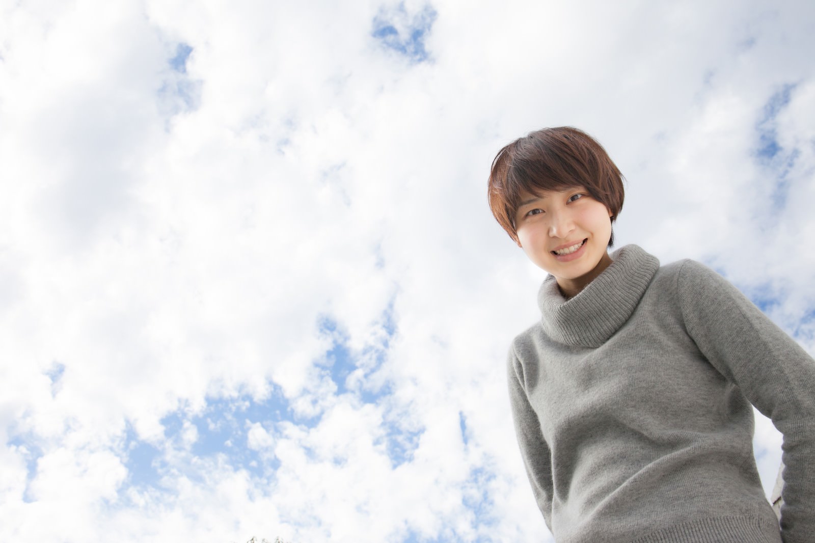 グレーのタートルネック姿で空を見上げて微笑む女性［モデル：八木彩香］