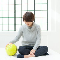 恋人はサッカーボール、グレーのニットセーター姿で床に座る女性の写真