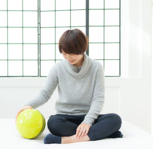 恋人はサッカーボール、グレーのニットセーター姿で床に座る女性