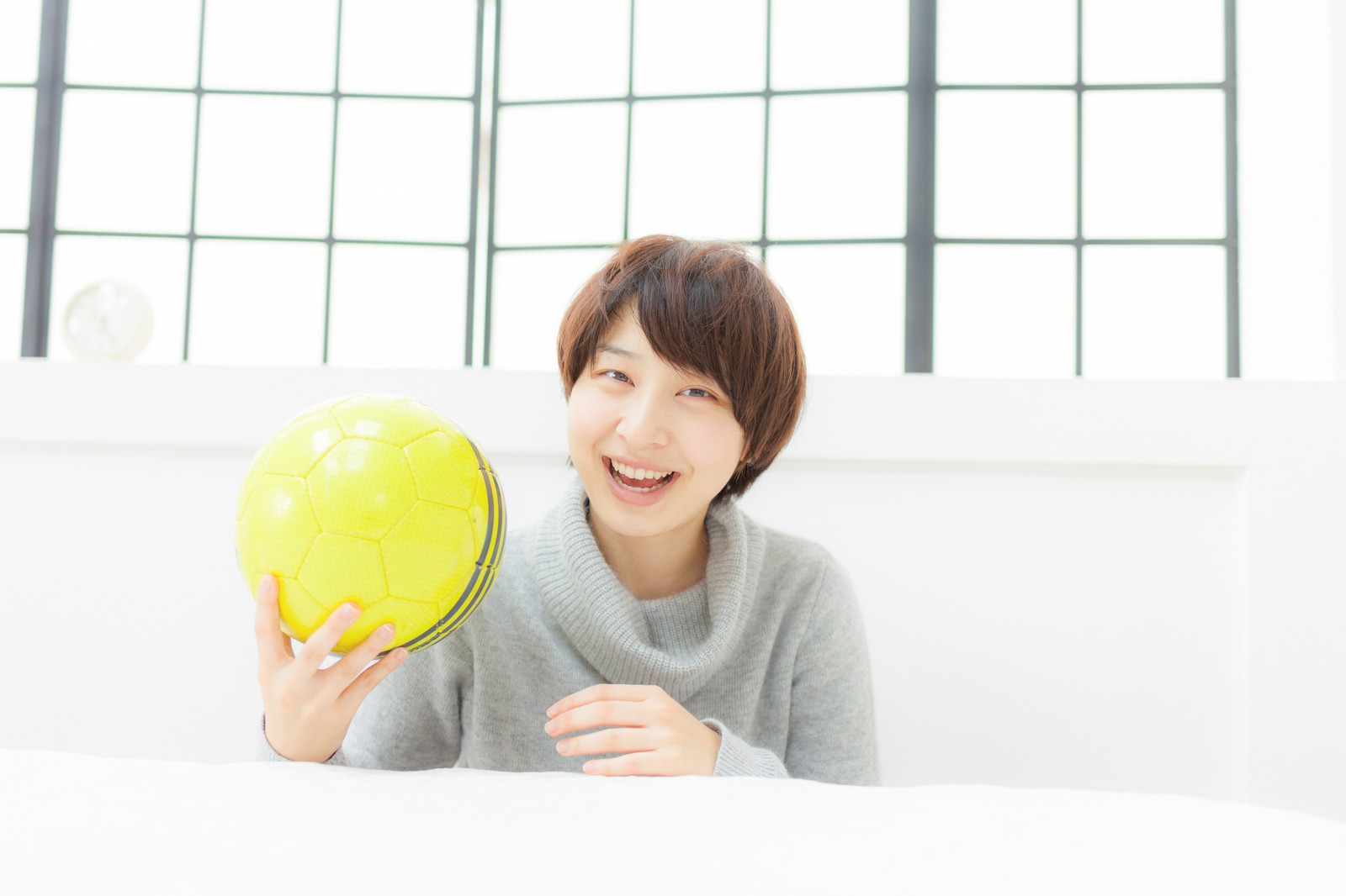 黄緑色のサッカーボールを両手で持ち笑顔を見せる女性［モデル：八木彩香］
