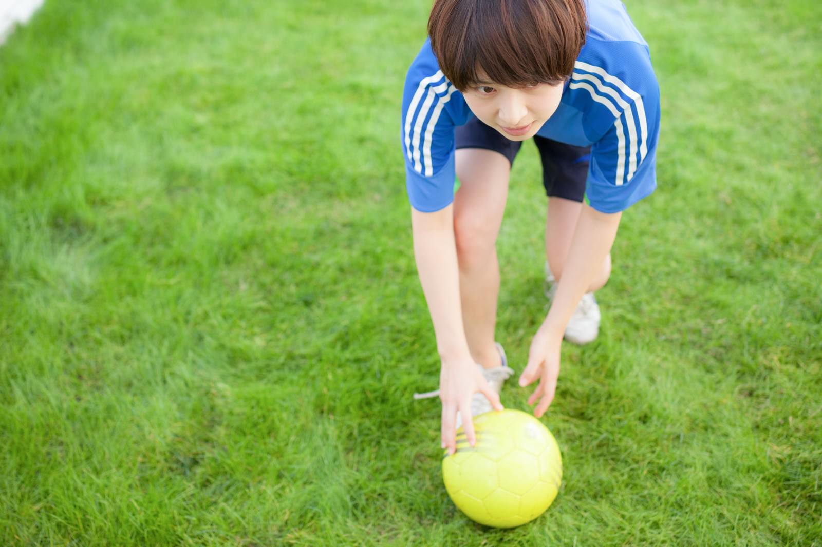 芝生の上で黄色いサッカーボールを置く子ども［モデル：八木彩香］