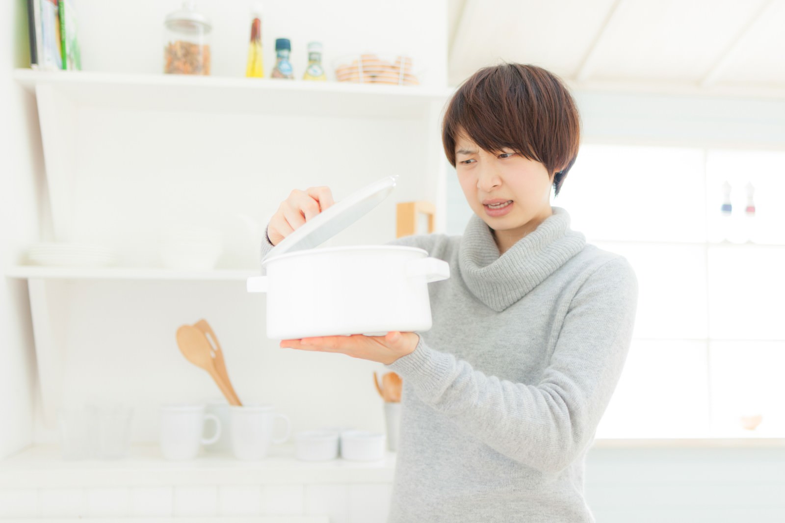 キッチンで鍋から異臭がして困った表情の女性［モデル：八木彩香］