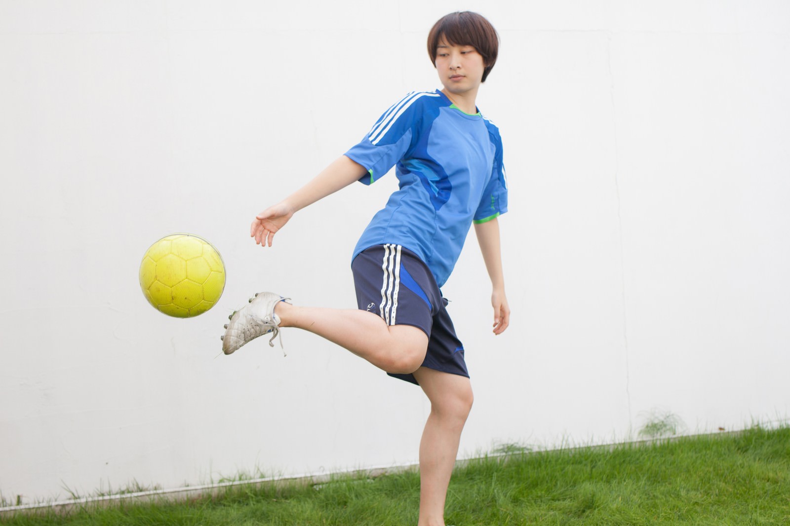 青いユニフォーム姿でサッカーボールをリフティングする女性［モデル：八木彩香］