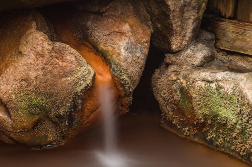 平湯温泉・栄太郎の源泉かけ流しから流れ落ちる湯と岩肌の温泉成分沈着