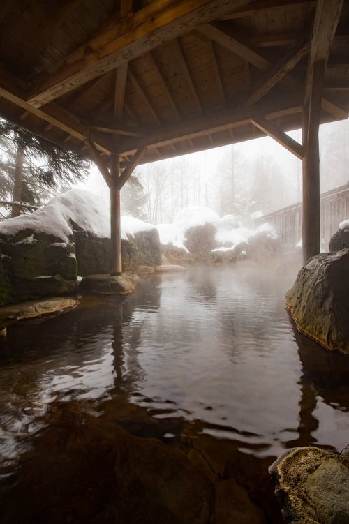 雪が降り積もる露天風呂、湯けむりが立ち上る冬の温泉風景