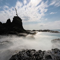 積丹町の海岸に打ち寄せる波と岩肌、流れる雲の風景の写真