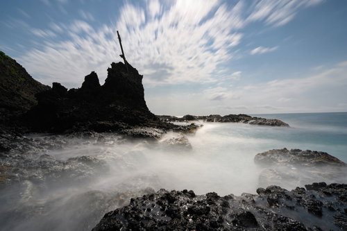 積丹町の海岸に打ち寄せる波と岩肌、流れる雲の風景