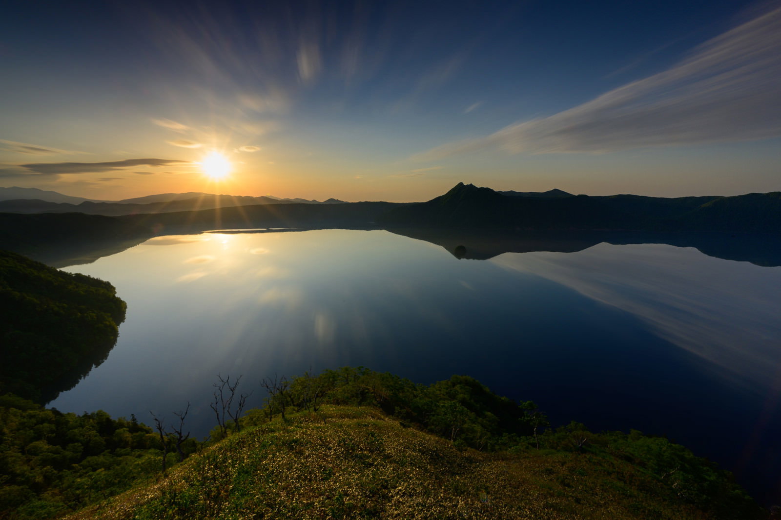 朝日が昇る摩周湖の風景、静かな湖面に朝焼けが反射している