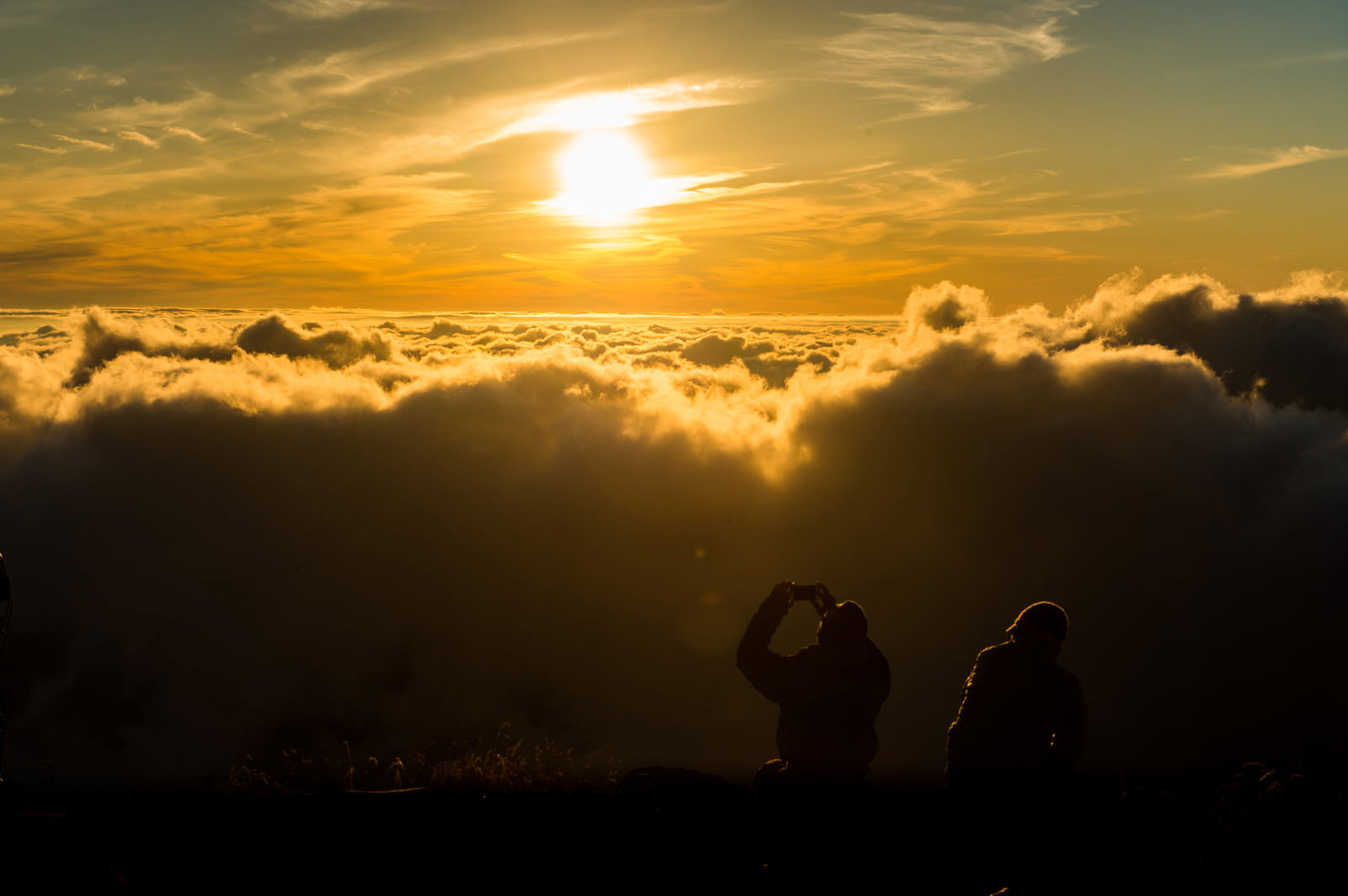 北アルプス山頂で夕日と雲海を背にシルエットで立つ2人