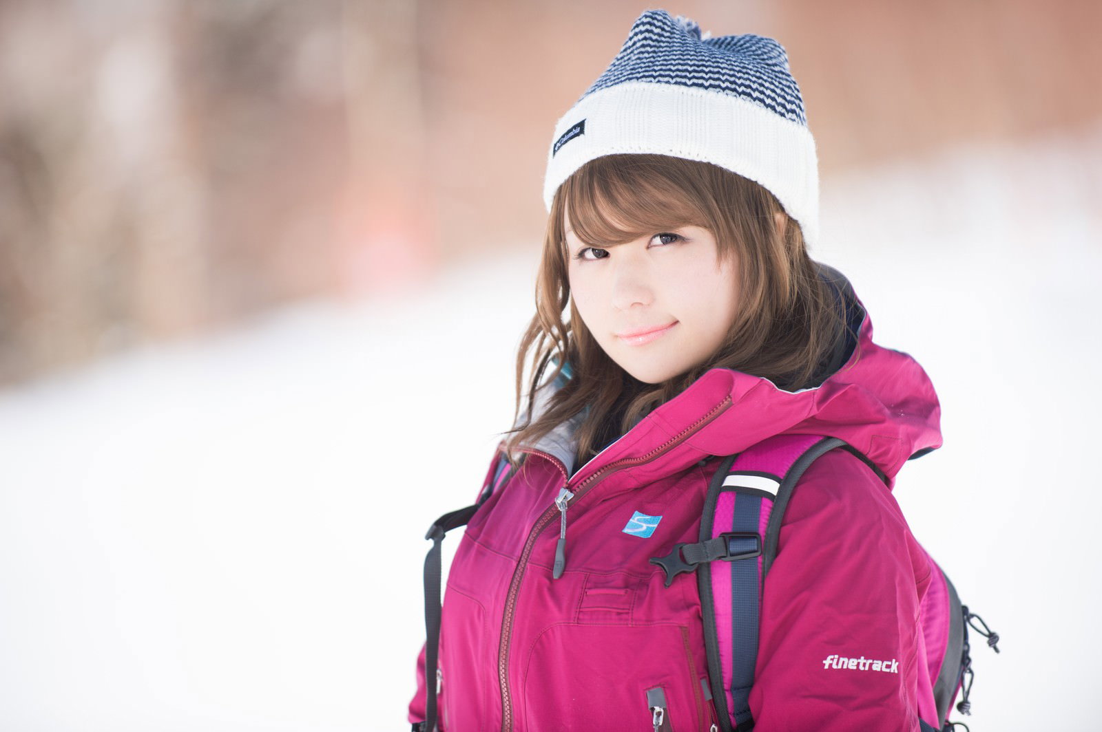 ピンクのジャケットとニット帽を着た女性が雪山に立つ［モデル：茜さや］