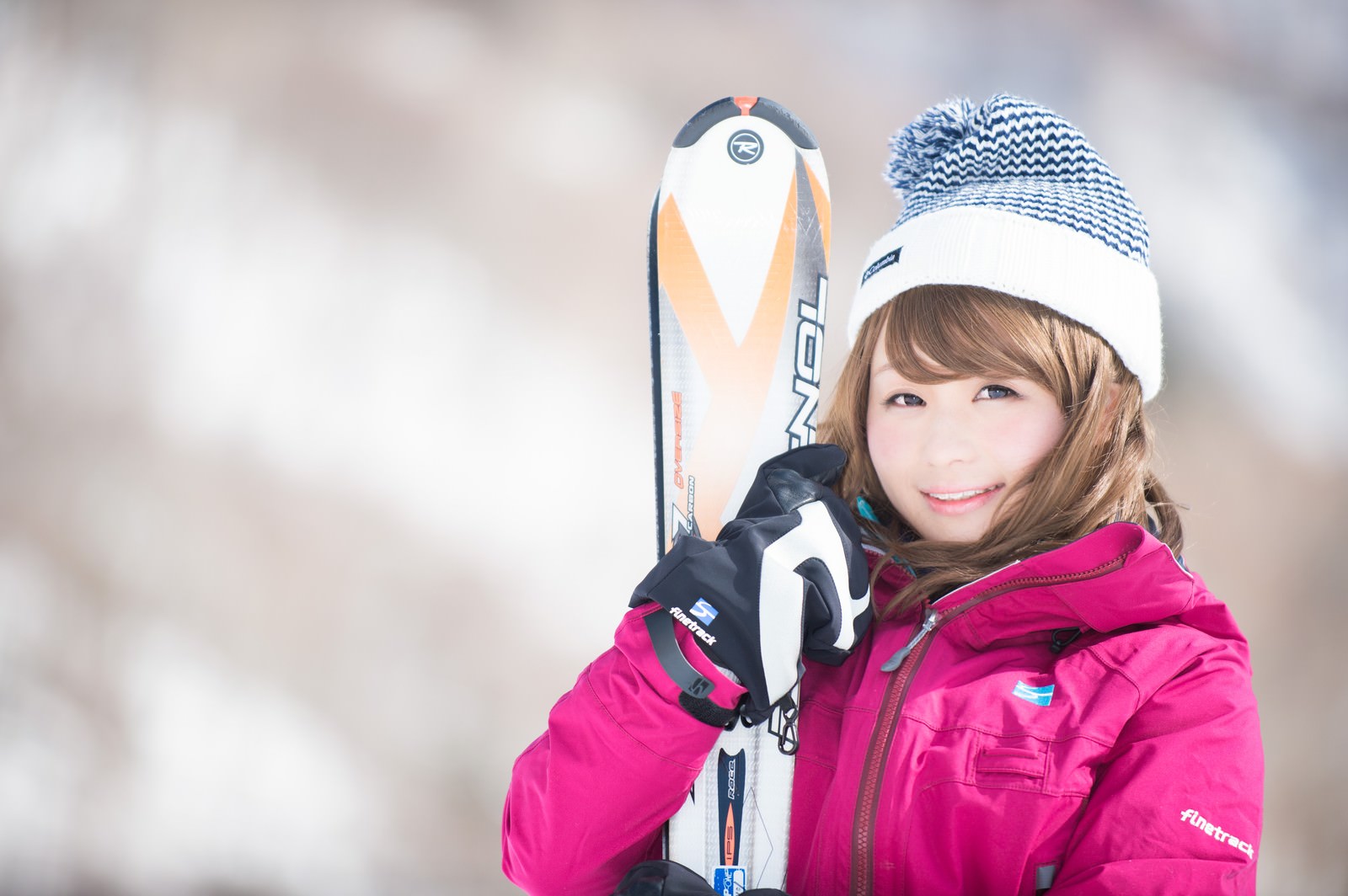 ピンクのスキーウェアとニット帽でスキー板を抱えて笑顔の女性のゲレンデポートレート［モデル：茜さや］