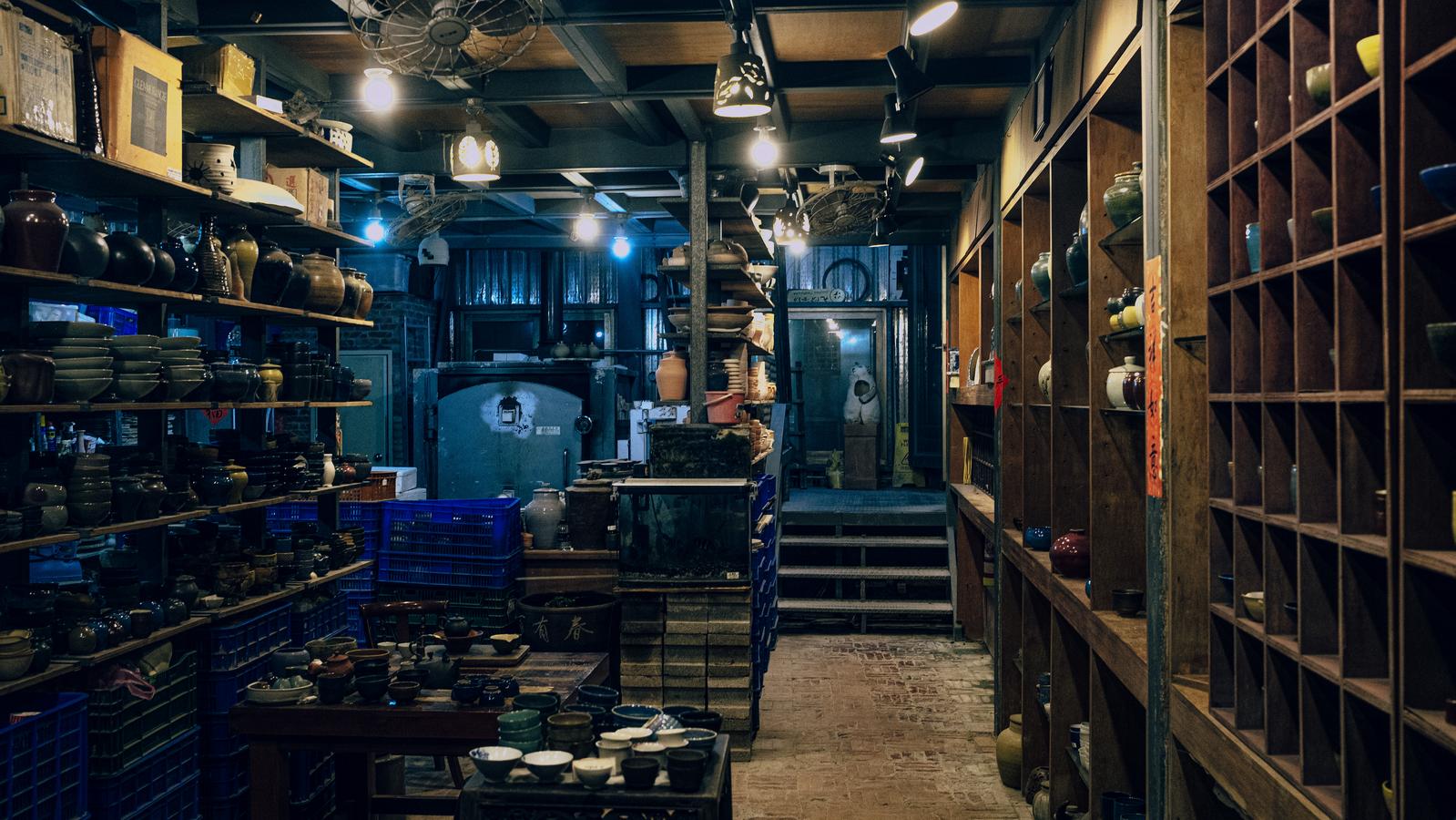 九份の陶器工房の夜間の店内。棚に陶器が並び、複数の照明が照らされている