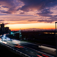 夕焼けに染まる空と車道に残る光跡、夜景の都市風景の写真