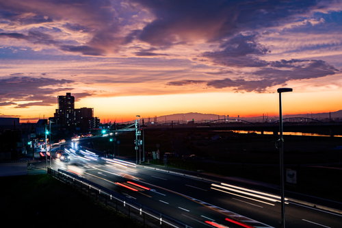 夕焼けに染まる空と車道に残る光跡、夜景の都市風景