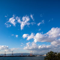 青空に浮かぶ白い雲と海沿いのコンビナートの写真