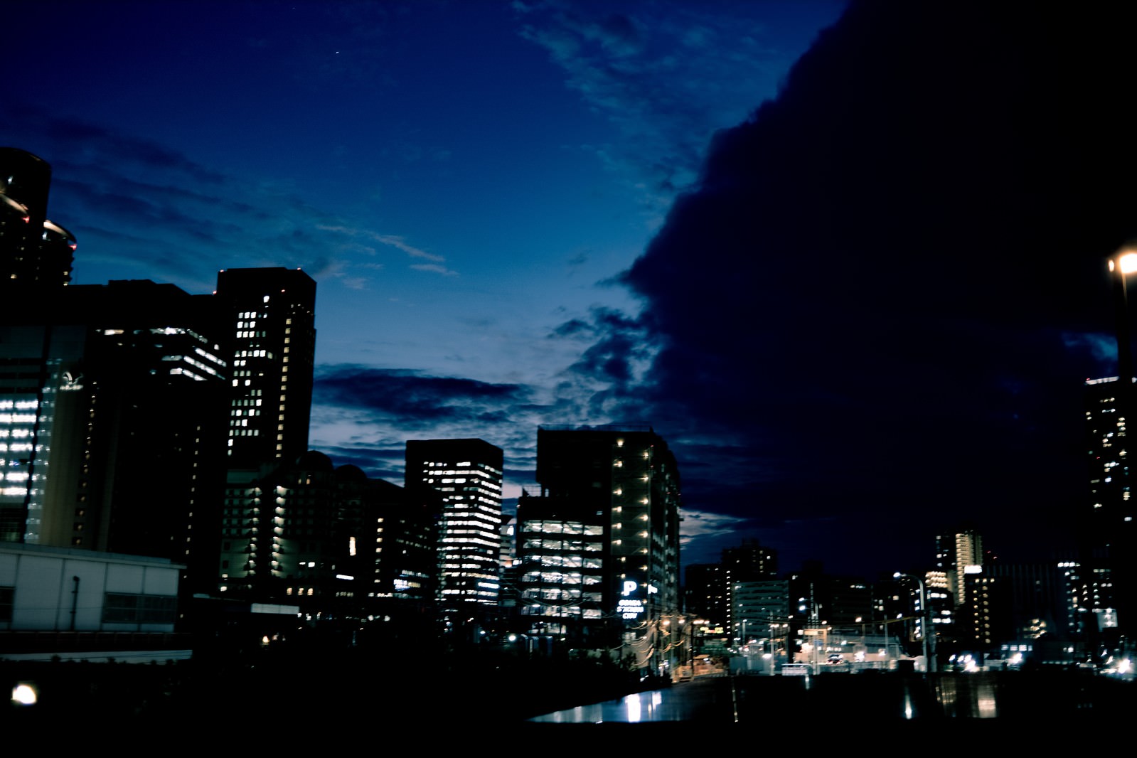 夜の街並みと雲空。高層ビルの窓明かりが輝く都市部の夜景