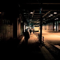 高架下の歩道でバス停留所に向かう人のシルエットの写真