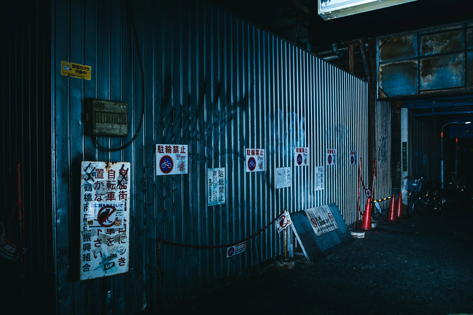 青いトタン壁に落書きと駐輪禁止の白い張り紙が貼られた夜の風景