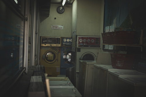 薄暗い蛍光灯の下に古い洗濯機が並ぶコインランドリー