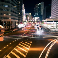 夜の交差点を行き交う車のヘッドライトとテールライトの光跡の写真