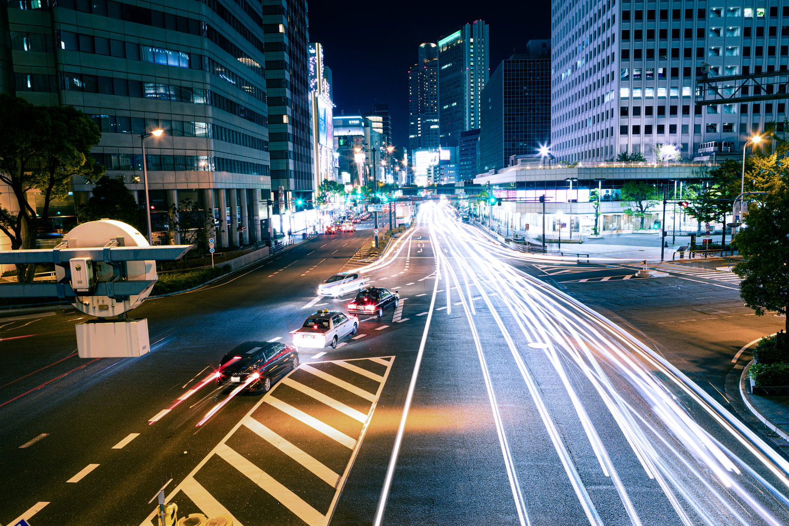 夜の交差点で車のライトが描く光跡と周囲のビル群
