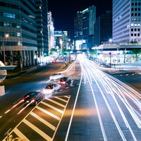 直進する車の光跡と右折レーンの車、夜の交差点の写真