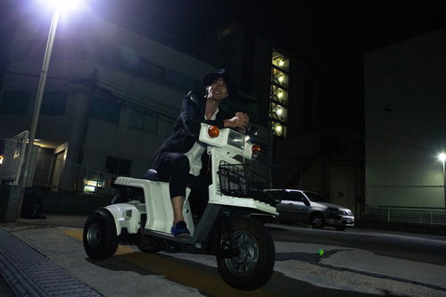 夜の街で原チャを乗り回す笑顔の男性、街灯に照らされた夜道での移動