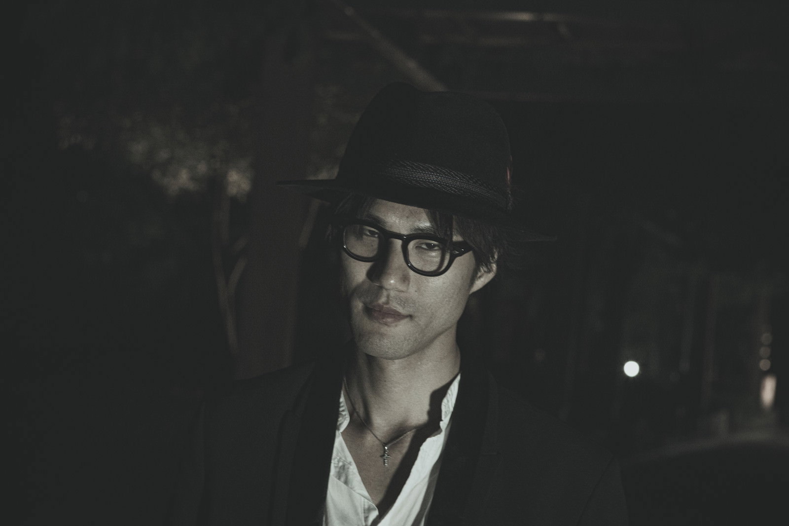 暗闇の中で眼鏡をかけた男性が正面を見つめている［モデル：村田裕章］