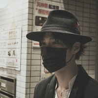 黒マスクと黒い帽子をして駅のホームを歩く出勤中の男性の写真