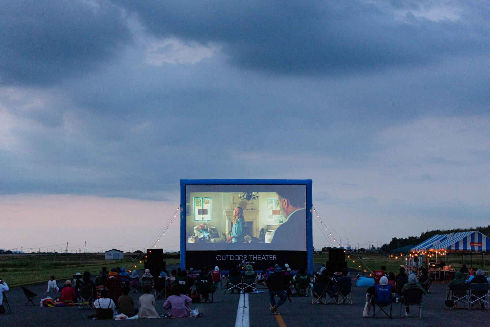 滑走路に設置された大型スクリーンで野外映画を鑑賞する観客たち
