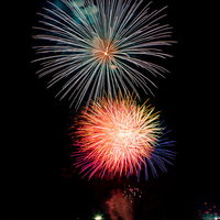 暗い夜空に炸裂するオレンジと青の打ち上げ花火の写真