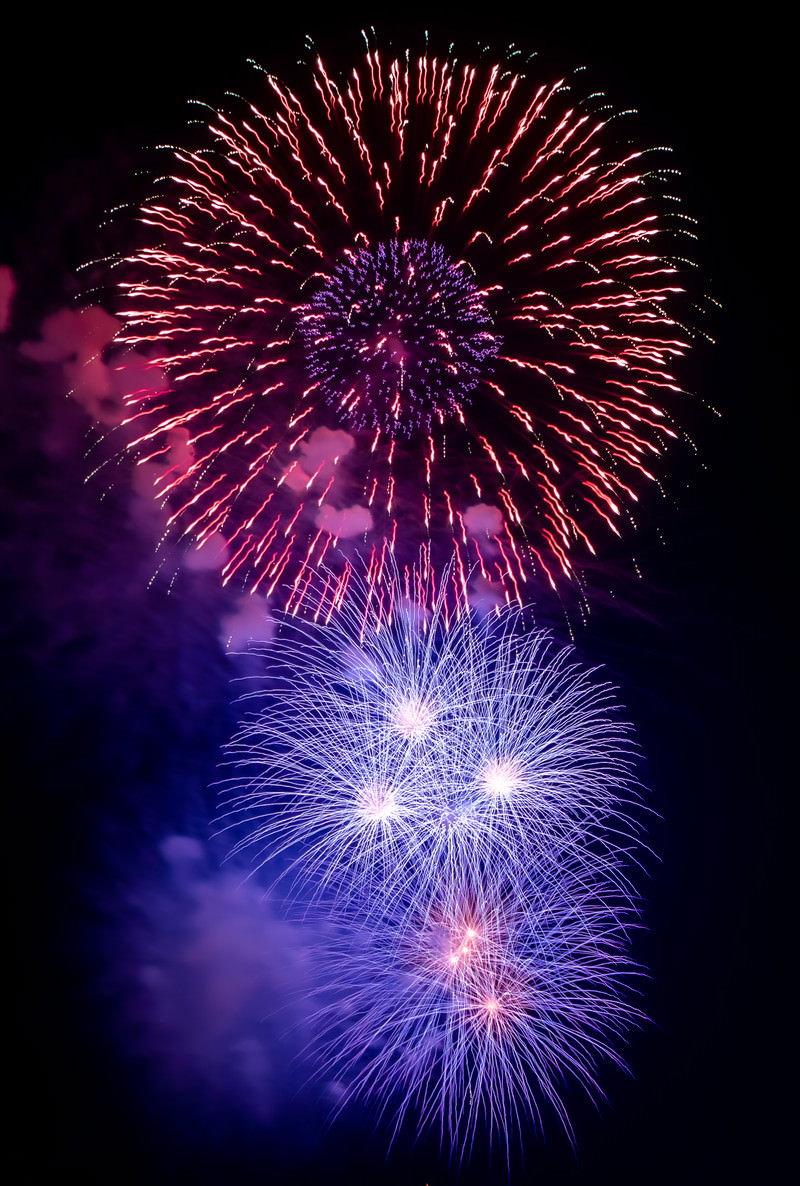 夜空に咲く大小の打ち上げ花火、紫とピンクと青の光が炸裂