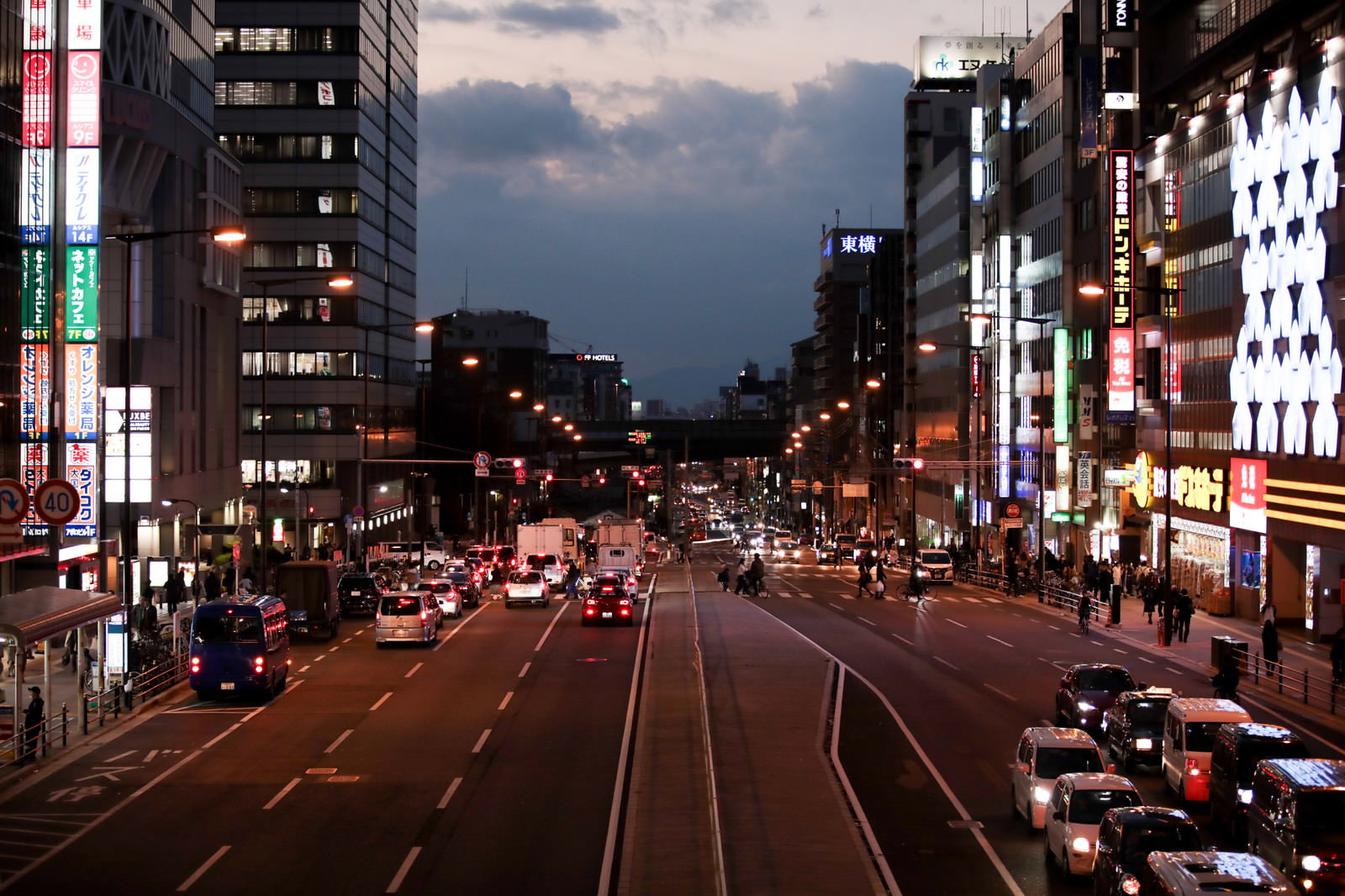 夕暮れの都市道路で赤信号により停止している車両と両側のビル群