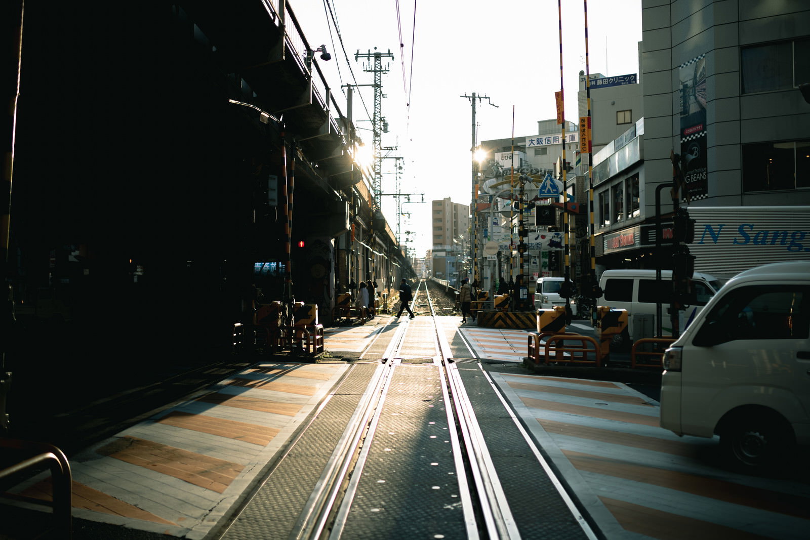 高架下へ続く踏切と線路、道路が交差する都市の交通風景