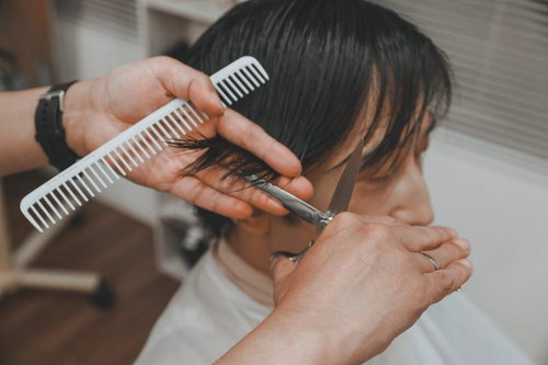 白いコームで髪をカットする美容師の手元とシザー