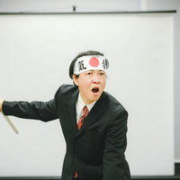 白いはちまきで竹刀を握り気合を入れるスーツの男性の写真