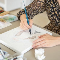 キャンバスに描いた図柄を筆で色付けしていく女性の写真