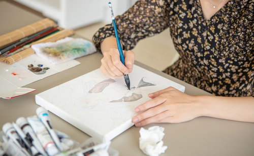 キャンバスに描いた図柄を筆で色付けしていく女性