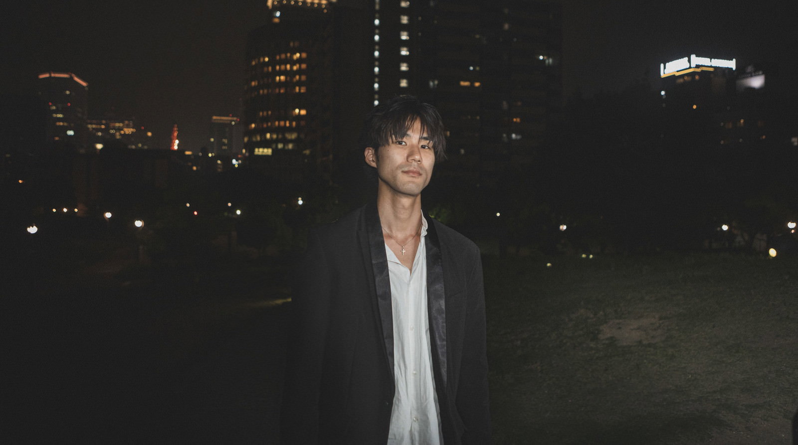 夜の街で白いシャツを着て立つ男性［モデル：村田裕章］