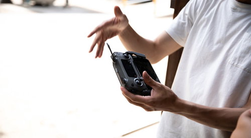 ドローンを操作する男性の手元、黒いコントローラーを操縦