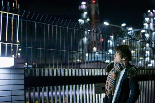 工場夜景を背景にマフラーを巻いた男性が待ち合わせで立つ