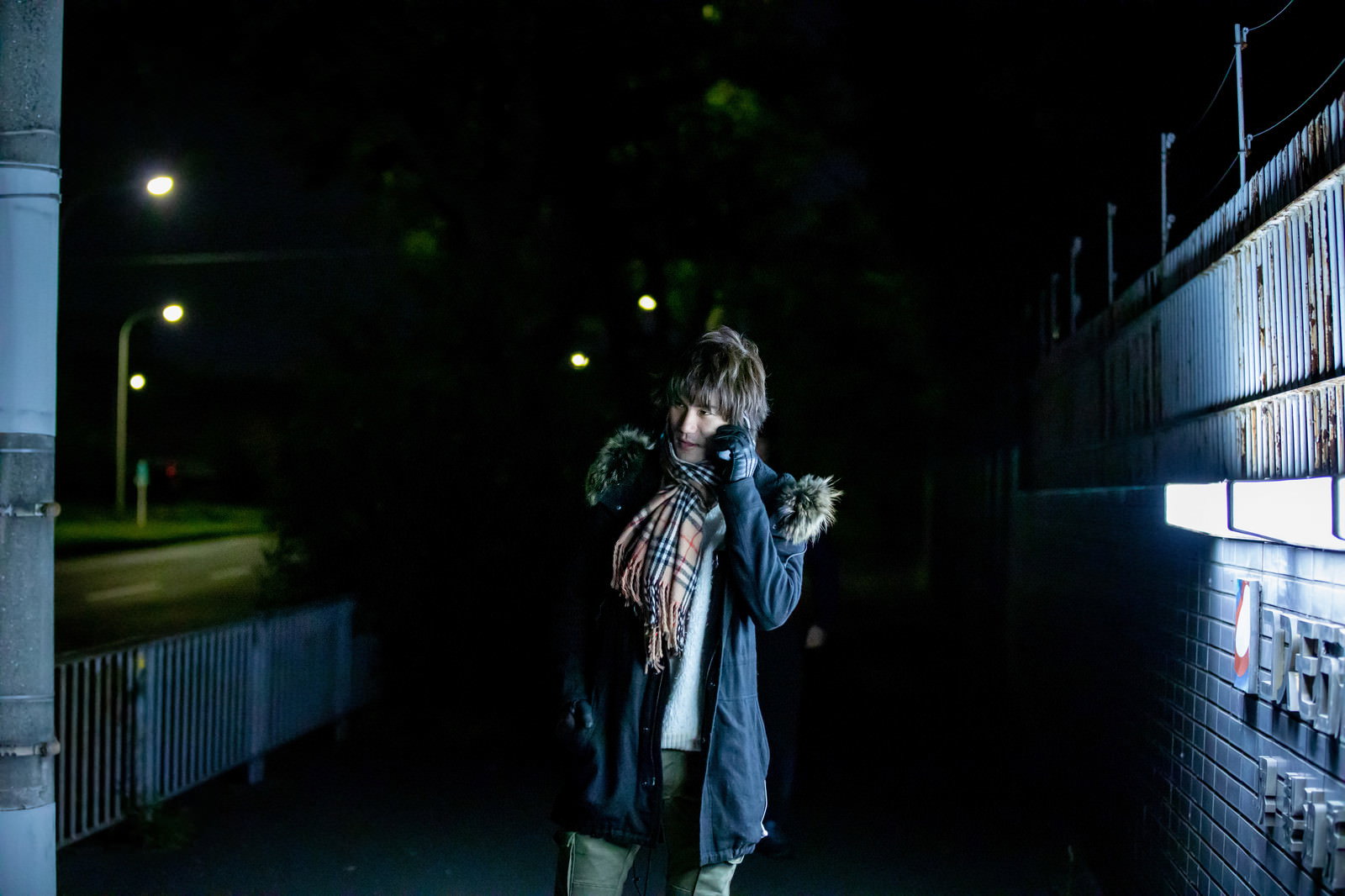 夜の暗い路地でスマートフォンを耳に当てて通話している男性［モデル：村田裕章］
