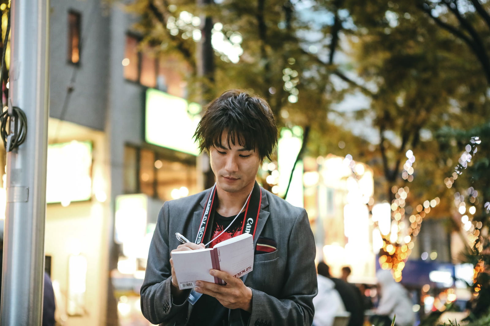夜の街中でスーツを着た男性がメモ帳に書き込みをしている様子［モデル：村田裕章］